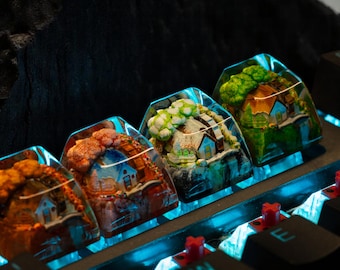 May include: Four miniature houses encased in clear resin keycaps, each with a different color scheme and design. The keycaps are arranged in a row on a black keyboard with blue LED lighting.