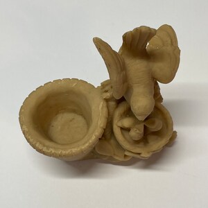 Peut inclure: Sculpture d&eacute;corative beige repr&eacute;sentant un oiseau aux ailes d&eacute;ploy&eacute;es au-dessus d'un petit r&eacute;cipient ouvert. La sculpture pr&eacute;sente un design sculpt&eacute; d&eacute;taill&eacute; et est faite d'un mat&eacute;riau solide.