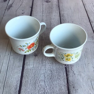 Coffee / tea cup. Corelle by Corning. Floral patterns. One yellow, one orange.