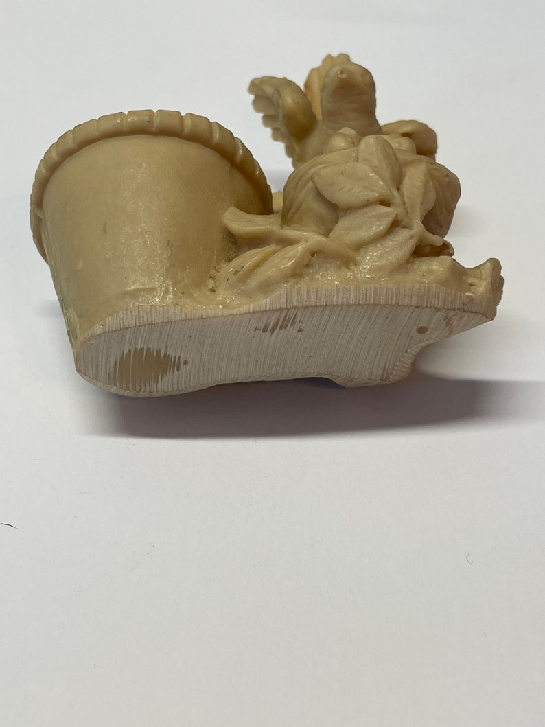 Peut inclure: Figurine beige repr&eacute;sentant un panier avec des fleurs et un oiseau. La figurine est faite d'un mat&eacute;riau de couleur claire et pr&eacute;sente des sculptures d&eacute;taill&eacute;es de feuilles et de p&eacute;tales. Le panier a un bord textur&eacute;.