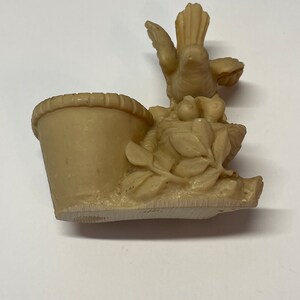 Peut inclure: Figurine beige repr&eacute;sentant un oiseau sur un nid avec un petit panier. L'oiseau a les ailes d&eacute;ploy&eacute;es et est entour&eacute; de feuilles et de petits fruits. Le panier est sur le c&ocirc;t&eacute; gauche.
