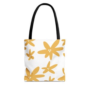 Peut inclure: Sac fourre-tout blanc orné d'un motif floral jaune répété. Le sac est doté de poignées noires et d'un design simple et moderne. Les fleurs ont trois petits points au centre. Le sac est probablement fabriqué dans un tissu durable.