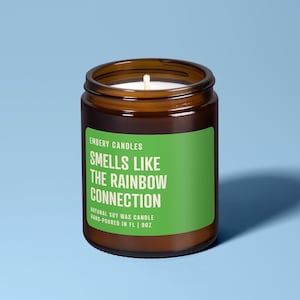 Può includere: Una candela in barattolo di vetro marrone con uno stoppino bianco. La candela ha un'etichetta verde con il testo "SMELLS LIKE THE RAINBOW CONNECTION". La candela è versata a mano in FL e contiene 255g di cera di soia naturale.
