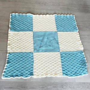 May include: A blue and white knitted baby blanket with a star design in the center.