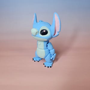 May include: A blue articulated figure of a cartoon character with large ears, a large eye, and a white nose. The figure has a light blue body with darker blue accents and black claws. The background is a gradient of pink and blue.