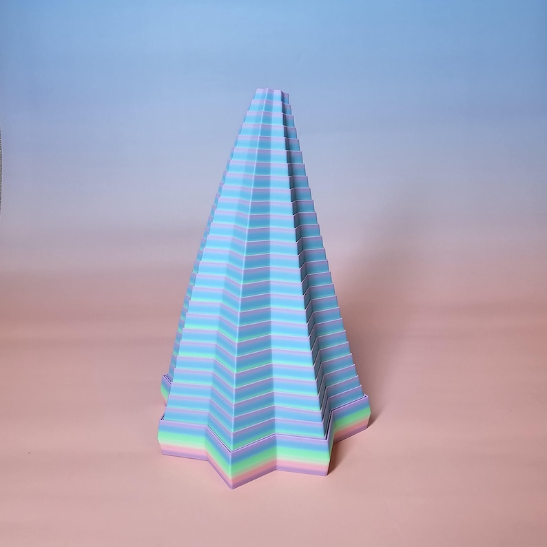 May include: A pastel-colored, geometric, cone-shaped sculpture. The sculpture features horizontal stripes of blue, purple, and green. The base is a five-pointed star. The artwork is set against a gradient background of pink and blue.