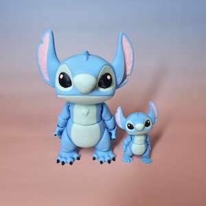 May include: Two blue Stitch figurines, one large and one small, are displayed together. The larger figure has articulated limbs and large ears with pink inner details. The smaller figure mirrors the design. Both have black eyes and a light blue belly.