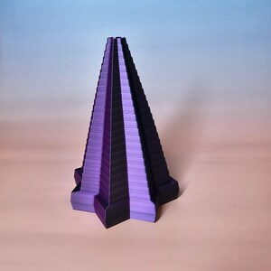 May include: A geometric, abstract sculpture in shades of purple and black. The piece has a layered, stepped design, resembling a stylized pyramid or tower. The sculpture is set against a gradient background.