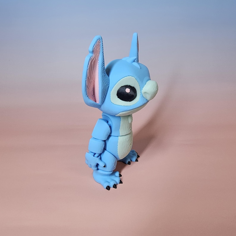 May include: A light blue articulated figurine of a cartoon character with large ears, a small nose, and large eyes. The figurine has a segmented body and black claws. The ears have pink inner details. The figurine is a popular character from a Disney animated film.