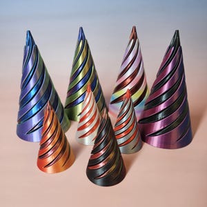 May include: A collection of seven decorative cone-shaped objects in various sizes and colors. The cones feature a spiral design with metallic finishes in shades of blue, green, red, orange, and black. The objects are arranged on a pink surface.