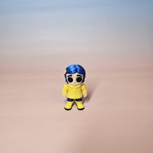 May include: A figurine of a character with blue hair, wearing a yellow jacket, blue pants, and yellow boots. The figurine has large black eyes and a small yellow star in its hair. The background is a gradient of pink and blue.