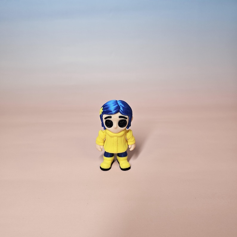 May include: A figurine of a character with blue hair, wearing a yellow jacket, blue pants, and yellow boots. The figurine has large black eyes and a small yellow star in its hair. The background is a gradient of pink and blue.