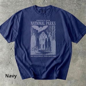 May include: Navy blue t-shirt with a graphic that reads "PROTECT OUR NATIONAL PARKS" above an illustration of forest creatures. The text "OR WE'LL HAUNT YOUR BACKYARD" is below the illustration.