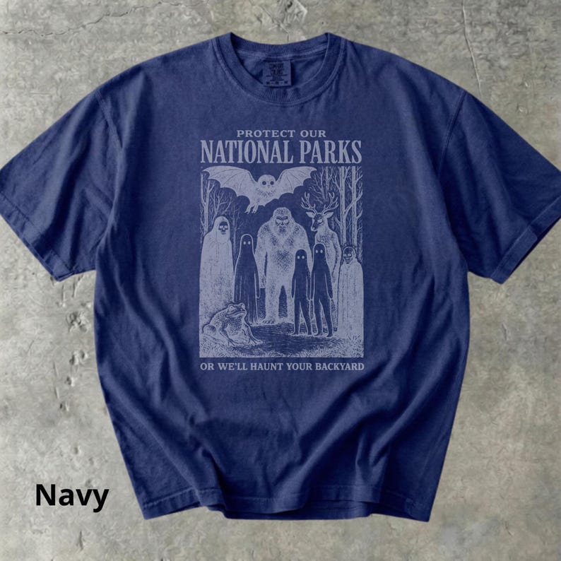 May include: Navy blue t-shirt with a graphic that reads "PROTECT OUR NATIONAL PARKS" above an illustration of forest creatures. The text "OR WE'LL HAUNT YOUR BACKYARD" is below the illustration.