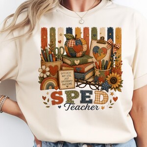 Può includere: Una t-shirt color crema con una stampa grafica di libri impilati, una mela patchwork, un portamatite, occhiali e un cartello con la scritta DIFFERENT NOT LESS, JUST DIFFERENTLY AWESOME. Il testo SPED Teacher è stampato sotto il grafico.