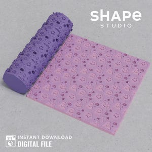Może przedstawiać: Wyświetlany jest fioletowy wałek do ciasta i różowy arkusz z wzorem. Wałek jest cylindryczny z teksturowaną powierzchnią. Arkusz ma powtarzający się wzór uśmiechniętych postaci przypominających duchy, gwiazd i chmur. Widoczny jest tekst "SHAPE STUDIO".