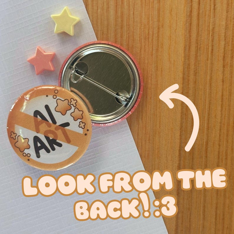 May include: A round button with the text "AI ART" crossed out, surrounded by star graphics. The back of the button is visible, along with two star-shaped embellishments. The text "LOOK FROM THE BACK! :3" is also present.