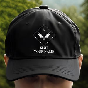 May include: Black baseball cap with a white diamond-shaped patch featuring a Roman numeral IV and wings. The text "CADET" and "[YOUR NAME]" are printed below the patch.