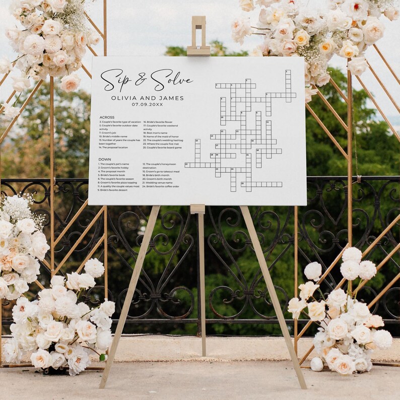 Large sip and solve wedding crossword puzzle displayed on an easel among white floral wedding arrangements. Perfect as a custom puzzle game sign for wedding receptions or bridal showers.