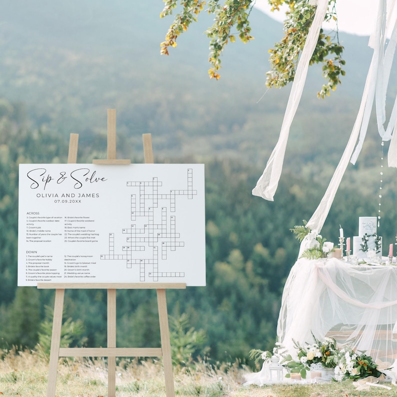 Personalized wedding crossword puzzle sign on an easel outdoors with mountain views and soft wedding décor. Fun and interactive sip and solve wedding table game for guests.