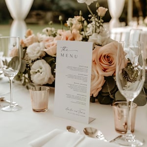 A sleek and elegant wedding menu card displayed on a beautifully set table, featuring roses and candles, showcasing the appetizer, main course, and dessert details. Perfect for adding sophistication to your wedding reception.