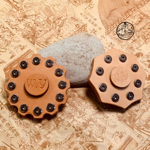 May include: Two leather fidget spinners with silver metal accents. The spinners are brown and have the letters "W.y" on them.