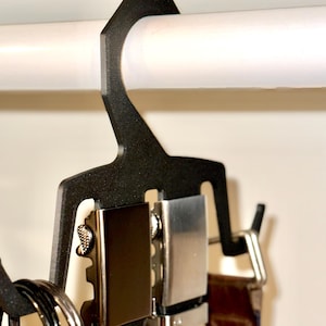 May include: A black plastic belt hanger with four belts hanging from it. The belts are brown, black, cream, and blue. The hanger has a hook at the top to hang it on a closet rod.