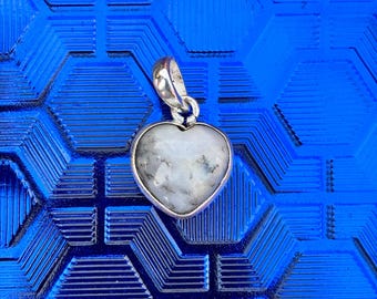 May include: A heart-shaped pendant with a silver-colored bail. The pendant features a white stone with gray and black marbling. The pendant is set against a textured, blue background.