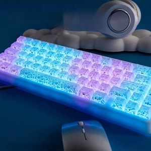 Könnte beinhalten: Eine weiße mechanische Tastatur mit blauer und violetter Hintergrundbeleuchtung. Die Tasten haben ein Riss-Eis-Design und die Tastatur hat einen weißen Rahmen.