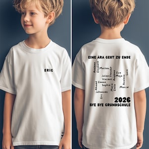 May include: White t-shirt with the name "ERIC" printed in black on the front. The back of the shirt features the text "EINE ÄRA GEHT ZU ENDE" and a list of names, along with "2026" and "BYE BYE GRUNDSCHULE".