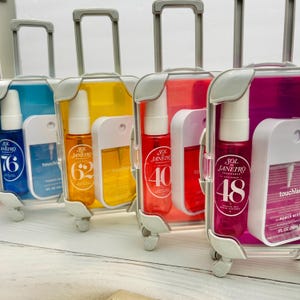May include: Four miniature suitcase-shaped cases containing Sol de Janeiro fragrance mists and Touchland power mists. The sets are blue, yellow, red, and pink, each featuring a spray bottle labeled with numbers 76, 62, 40, or 48 and a 1 fl. oz. sanitizer.