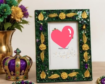 May include: A rectangular photo frame with a dark green glittery surface, decorated with gold-colored leaf and rose embellishments and purple accents. The frame contains a white insert with a pink heart graphic and the text Photo Frame.