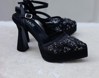 May include: Black high-heeled platform sandals with a delicate beaded design and an ankle strap with a buckle closure. The brand name "Ainlik" is visible on the shoe.