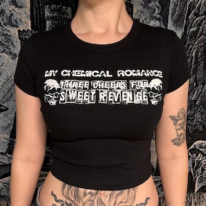 Może przedstawiać: Czarny top z białym napisem "MY CHEMICAL ROMANCE THREE CHEERS FOR SWEET REVENGE". Koszulka ma okrągły dekolt i krótkie rękawy. Tekst zawiera grafikę czaszki.