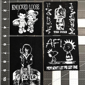 May include: Four black patches with white graphics and text. One patch reads "KNOCKED LOOSE" with two cartoon figures. Another says "THE CURE". A third patch has "FCKER" on a tombstone. The last patch says "AFI" with Snoopy and a cartoon figure.