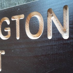 May include: A black wooden sign with the word "INGTON" carved into it in white.
