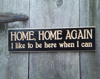 May include: Black wooden sign with the text "HOME, HOME AGAIN I like to be here when I can" in gold lettering.