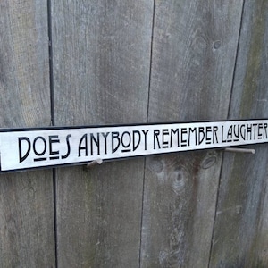 May include: A black and white wooden sign with the text "DOES ANYBODY REMEMBER LAUGHTER?" in a stylized font.