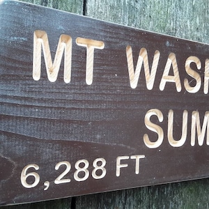 May include: A dark brown wooden sign with white lettering that reads "MT WASHING SUMMIT 6,288 FT".