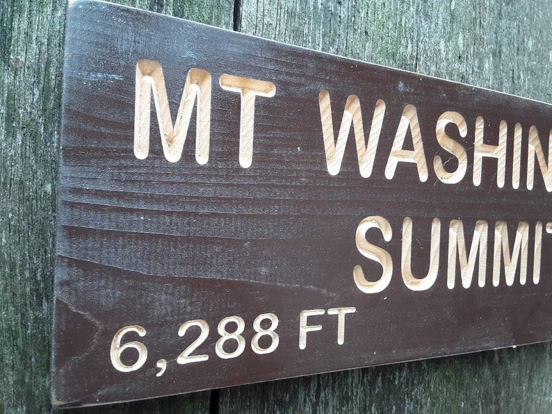 May include: A dark brown wooden sign with white lettering that reads "MT WASHING SUMMIT 6,288 FT".