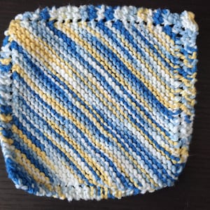 Puede incluir: Paño de lavado cuadrado tejido a mano con rayas diagonales en tonos de azul, blanco y amarillo. Los bordes están acabados con un borde azul contrastante. Este artículo hecho a mano es perfecto para la cocina o el baño.