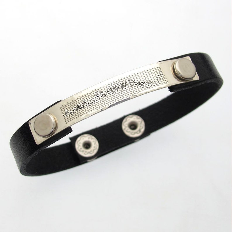 May include: A black leather bracelet with a silver plate engraved with a heart rate line. The bracelet has three silver snaps.