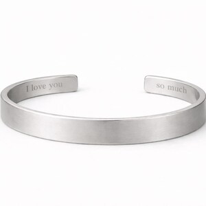 May include: A silver-toned metal cuff bracelet with a brushed finish. The interior surface of the open-ended band features the engraved text I love you on the left side and the text so much on the right side of the opening.