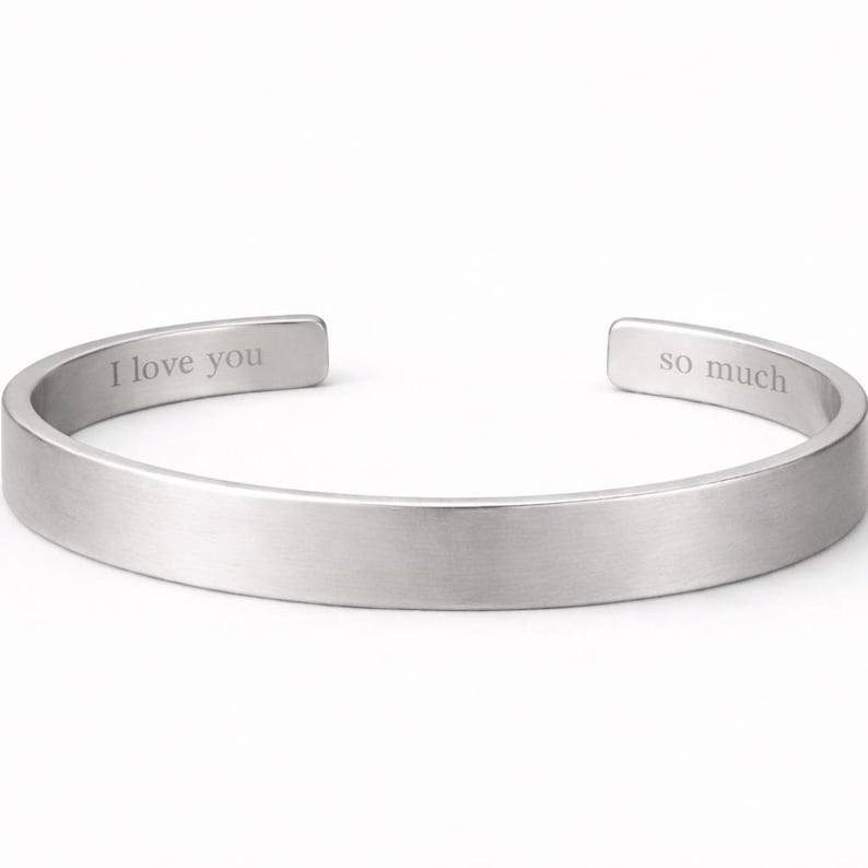 May include: A silver-toned metal cuff bracelet with a brushed finish. The interior surface of the open-ended band features the engraved text I love you on the left side and the text so much on the right side of the opening.