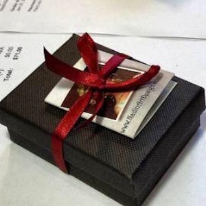 May include: A small black gift box with a red ribbon tied around it. The box has a white card attached to it with the text "www.haddonhilldesigns.co.uk".