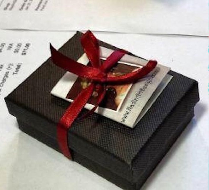 May include: A small black gift box with a red ribbon tied around it. The box has a white card attached to it with the text "www.haddonhilldesigns.co.uk".