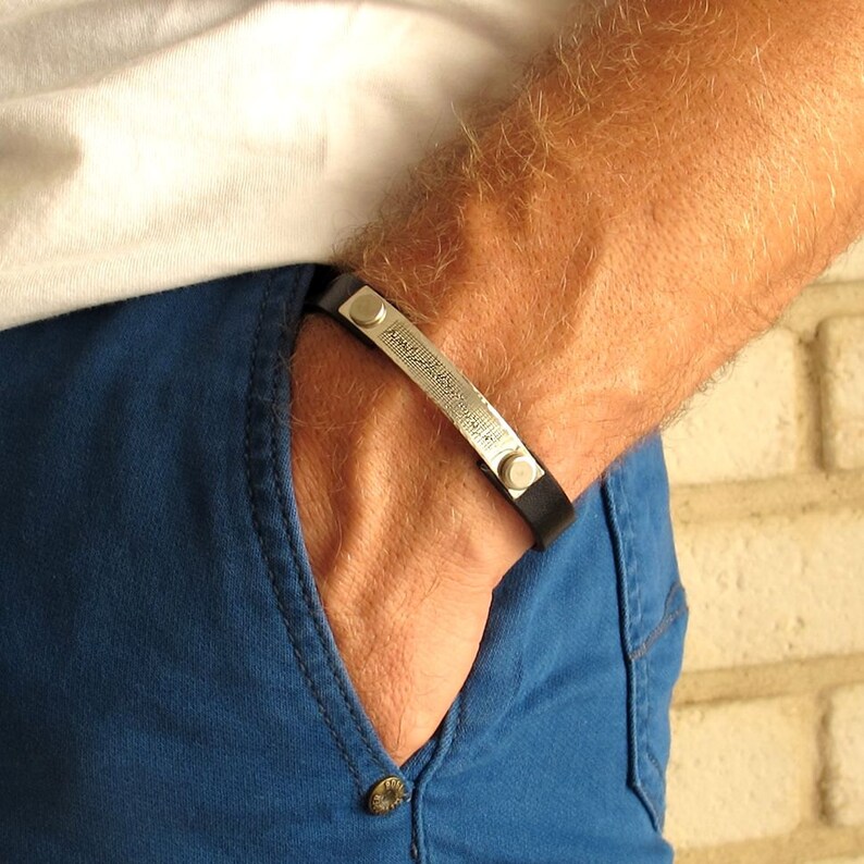 May include: A black leather bracelet with silver accents and a textured silver band. The bracelet is worn on a person's wrist.