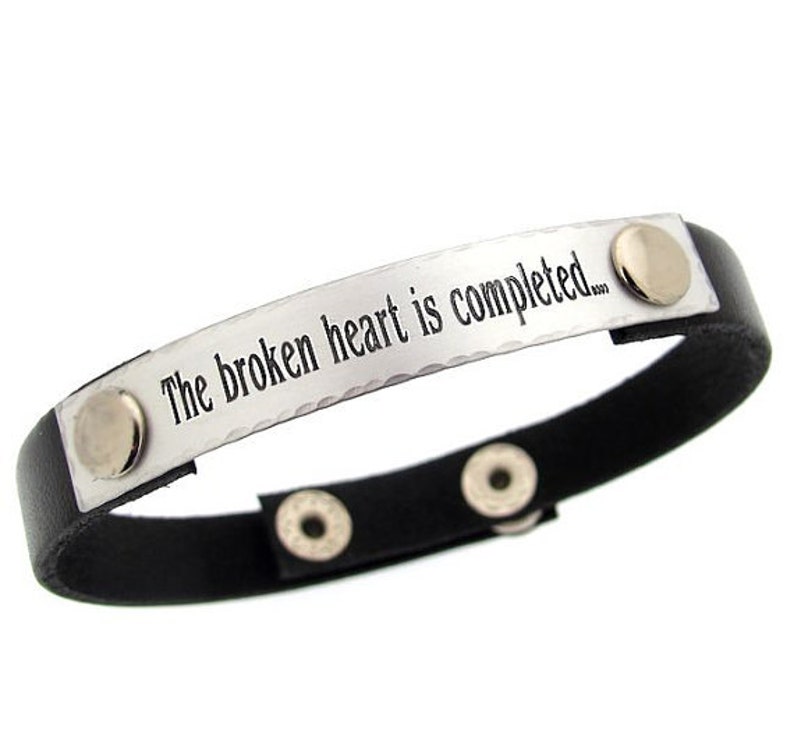 May include: A black leather bracelet with a silver metal plate engraved with the words "The broken heart is completed..."