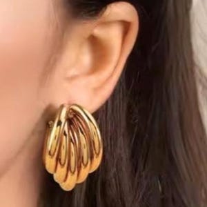 Puede incluir: Pendientes dorados con dise&ntilde;o de capas, con un dise&ntilde;o en forma de concha. Los pendientes son de estilo clip y tienen una superficie pulida y reflectante. La joyer&iacute;a es un accesorio audaz.