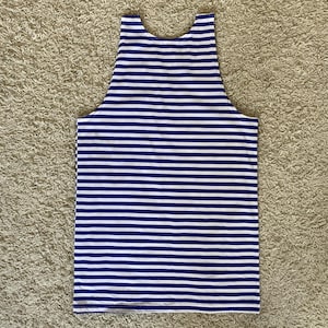 May include: A sleeveless tank top with horizontal blue and white stripes. The top has a scoop neckline and a straight hemline. The fabric appears to be a lightweight material, suitable for warm weather.